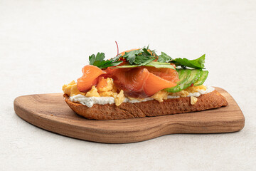 Breakfast toast with salmon and avocado on wooden board