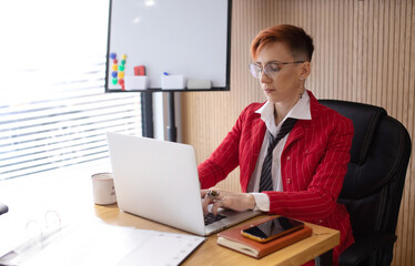 Shot of an attractive mature businesswoman in red suit working on laptop in her workstation.