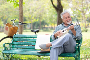senior man playing ukulele and looking forward in a park