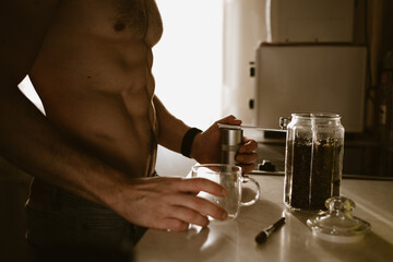 A naked man prepares coffee in the kitchen in the morning