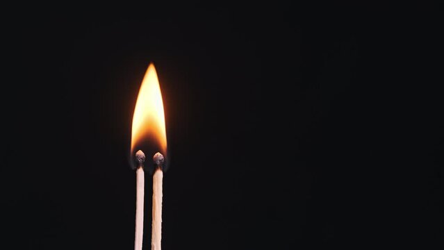 Two matchsticks ignites and burns on a black background close-up, copy space. Igniting match sulfur. Match sticks magically lighting and lit. Fire flame. 4K, 59,94fps.