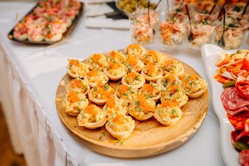 Riga, Latvia - January 18, 2024 - Tartlets filled with cream and topped with caviar on a wooden board, part of a catering spread.