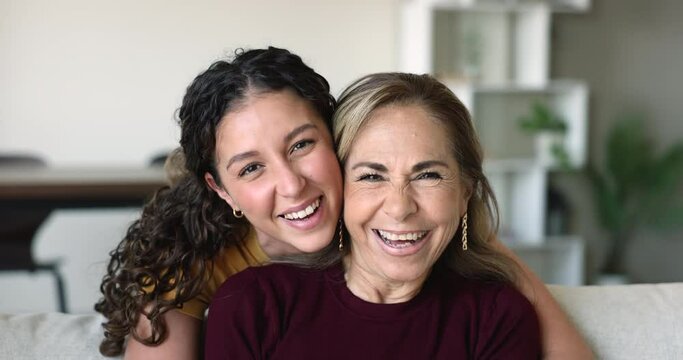 Two beautiful laughing female hugging staring at camera. Close up portrait of multigenerational relatives women, young adult daughter cuddle her older mother posing for cam. Family moments, love, ties