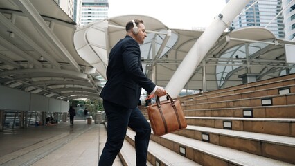 Smart caucasian businessman walking up stairs surrounded by urban view. Back view of happy...