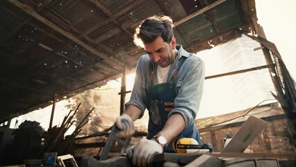 A handsome male craftsman was sawing wood with a saw with great concentration, A carpenter is doing a business making wooden furniture in a wood shop