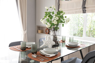 White and brown plate setting on dinning table with flowers vase in a dining room