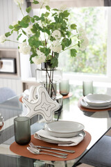 White and brown plate setting on dinning table with flowers vase in a dining room
