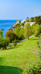Fototapeta na wymiar Genoa, Italy. View of the sea with a meadow in the Nervi Park in the foreground, with a tree-lined avenue. In the distance the Gropallo Tower overlooking the sea. Vertical image. 2023-10-06.