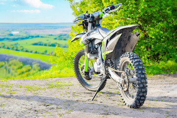 an extreme cross enduro motorcycle stands on a hill overlooking a field and a blue sky with clouds. concept of traveling through nature on a motorcycle. close-up