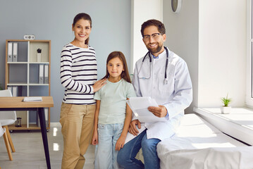 Girl patient with her mother standing at doctor's office in clinic on consultation with friendly...