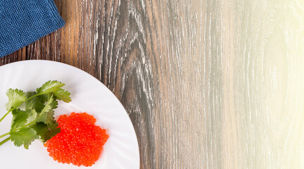 Red caviar on a white plate with herbs on the wooden table on sunlight
