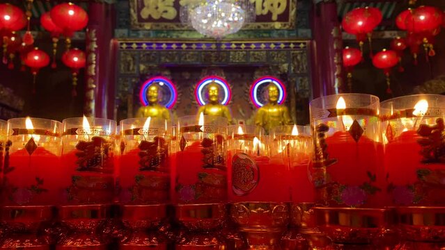 Worshippers light candles in front of golden Buddha images during the Chinese Lunar New Year celebrations at Wat Mangkon temple in Bangkok China town, Thailand.