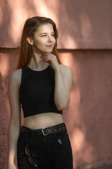 Portrait of a young beautiful long-haired girl in dark clothes on a summer street.