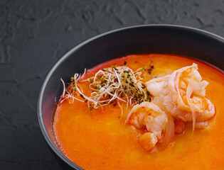 Traditional Thai soup Tom Yam in black bowl