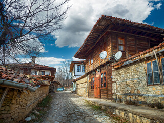 Zheravna, Bulgaria - narrow cobbled road and rustic traditional houses made of stone and wood with...