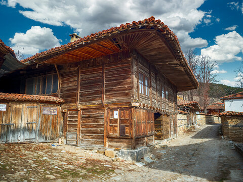 Zheravna, Bulgaria - narrow cobbled road and rustic traditional houses made of stone and wood with bigroot cranesbill (Geranium macrorrhizum) along the stone wall - Image
