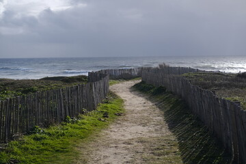 Obraz premium A small path through some wooden fence to reach the shore on a stormy day. Batz-sur-Mer, France - February 10, 2024.