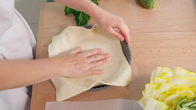 The chef puts the dough into a round pie pan on a wooden table. Close-up, side view.