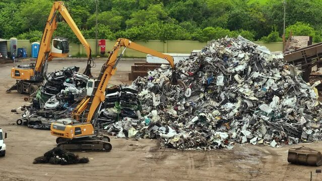 Old vehicle utilization junkyard with claw crane manipulator machines lifting and disposing cars for scrap metal. Transport equipment at crashed auto disposal site