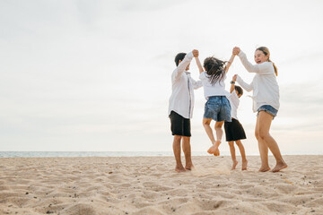 A burst of joy on beach as an Asian family father and mother holding children leaps into air....