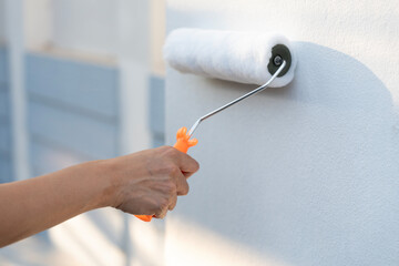 hand worker holding brush painting roller white on the wall house, diy and repair concept