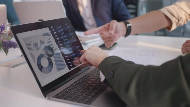 Business workers analyzing data on laptop screen, pointing on chart with hands close up. Company employees team checking analytics report statistics selective focus