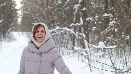 A young woman stands against a background of fir trees under a snowy forest in winter. A girl in a...