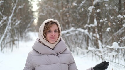 A young woman stands against a background of fir trees under a snowy forest in winter. A girl in a...