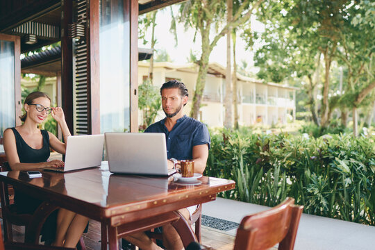 Coworking and freelance concept. Young  bearded man  and young woman working together on laptop computer while sitting on cafe terrace.