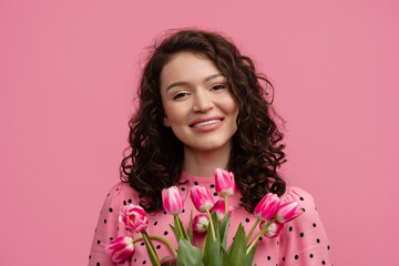 pretty young woman posing isolated on pink studio background with tulips flowers
