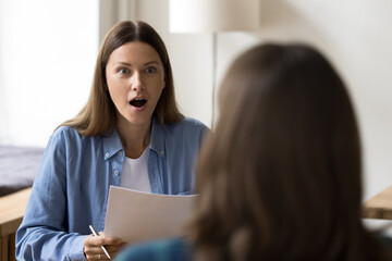 Shocked entrepreneur woman holding paper document, staring at female business colleague, project partner with open mouth. Job candidate surprising employer at interview - obrazy, fototapety, plakaty