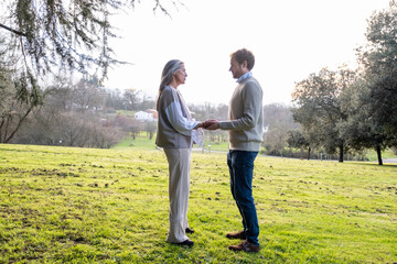 A woman and a middle-aged man practising neurodance in a green meadow in the nature of a park.