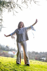 A middle-aged woman practising neurodance on a green lawn in the park at sunset.