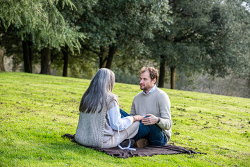 Naklejka na ściany i meble A man and a woman practising concentration exercises and spiritual connection sitting in a green meadow surrounded by trees in a park.