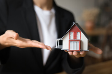 Property sales manager holding small model of house on palm, pointing hand at object, promoting property buying and selling, apartment rent service. Cropped close up shot