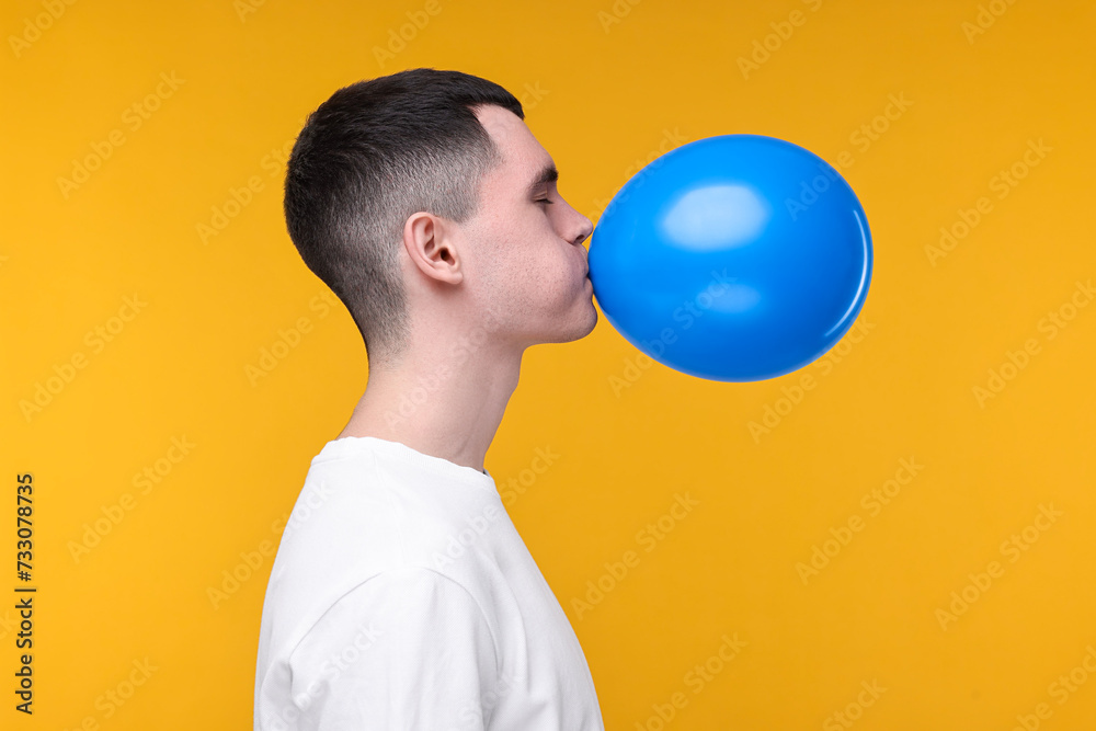 Canvas Prints Young man inflating light blue balloon on yellow background