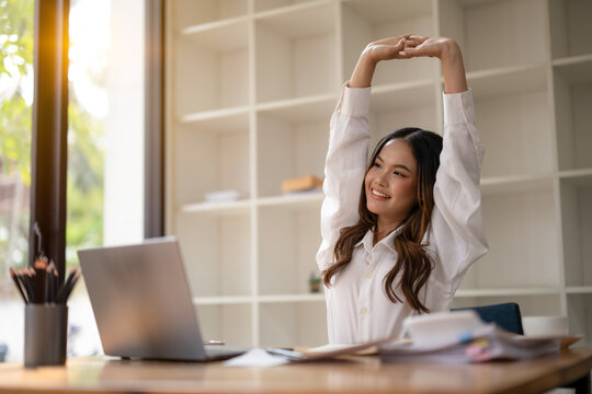 Young professional woman taking a stretching break at her office workspace, smiling with satisfaction.