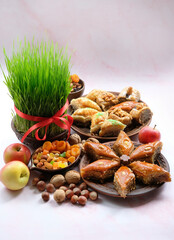 Nowruz holiday festive table. arabic dessert baklava, sweets, nuts, dry fruits, apples, green wheat grass with red ribbon on light pink background. celebration of spring equinox in March, Nowruz feast