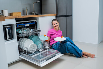 Young woman sitting on the floor near the dishwasher machine