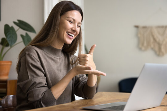 Happy communication expert speaking to patient with hearing disability online, showing thumb up on palm at computer, smiling, laughing. Sign language therapist using Internet for communication