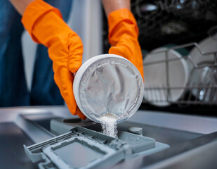 Woman adding detergent to dishwasher machine drawer