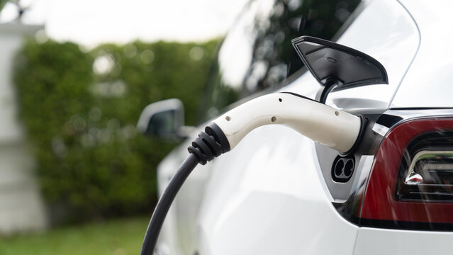 Closeup EV charger plug handle attached to electric vehicle port, recharging battery from charging station. Modern designed EV car and clean energy sustainability for better future concept. Synchronos