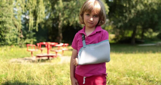 A small, handsome boy with a broken arm wrapped in a bandage. An injured child on the playground.