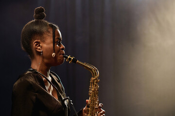 Minimal side view portrait of Black young woman playing saxophone music on stage in spotlight copy...