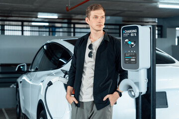 Young man travel with EV electric car to shopping center parking lot charging in downtown city...