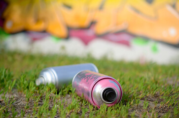 Several used spray cans with paint and caps for spraying paint under pressure on grass near the...