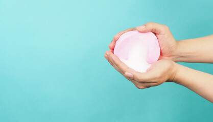 Hands washing gesture with pink sponge and foaming hand soap on mint green or tiffany blue background.