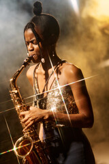 Fototapeta na wymiar Vertical portrait of talented young woman playing saxophone during jazz music concert with golden light accents