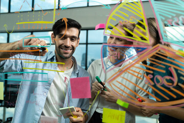 Skilled project manager pointing at glass wall while coworker thinking about plan. Diverse business team working together, brainstorming marketing idea or business plan. Creative start up. Tracery.