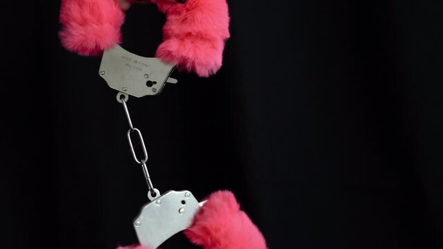 Pink fluffy handcuffs on the hands of a young girl. Toys from a sex shop for role-playing games of couples, love and hot sex in a romantic atmosphere